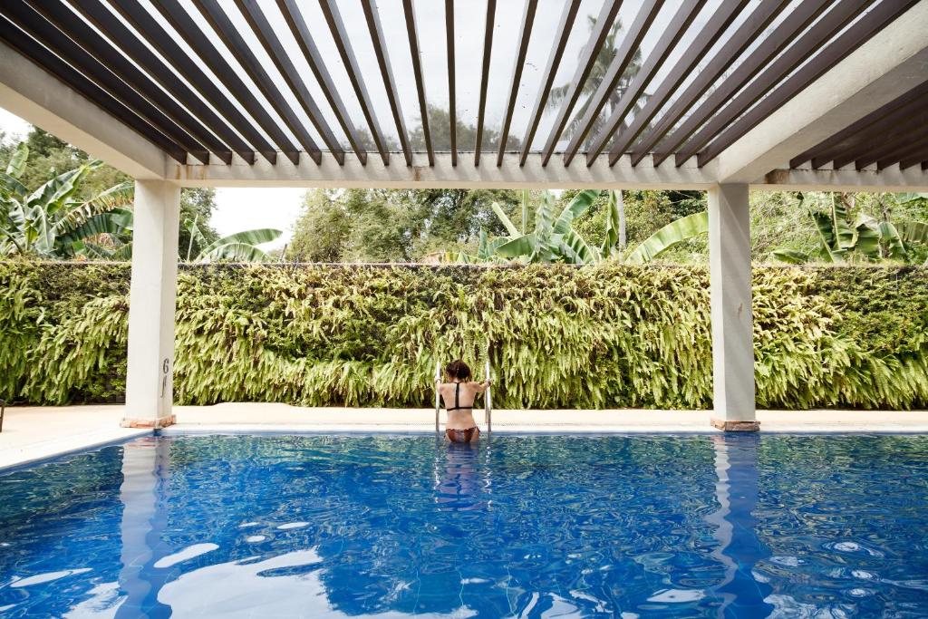 Guest swimming in Munting Paraiso's pool beneath a pergola lined with hanging ferns