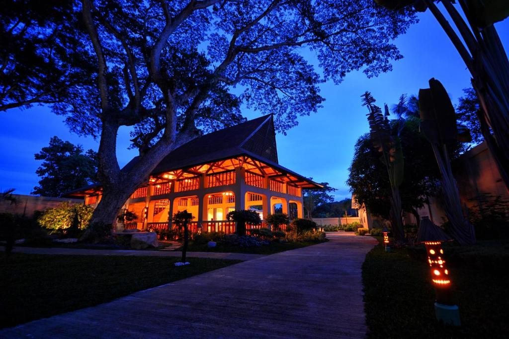 Munting Paraiso's main pavilion lit at dusk beneath a century-old acacia tree on the property