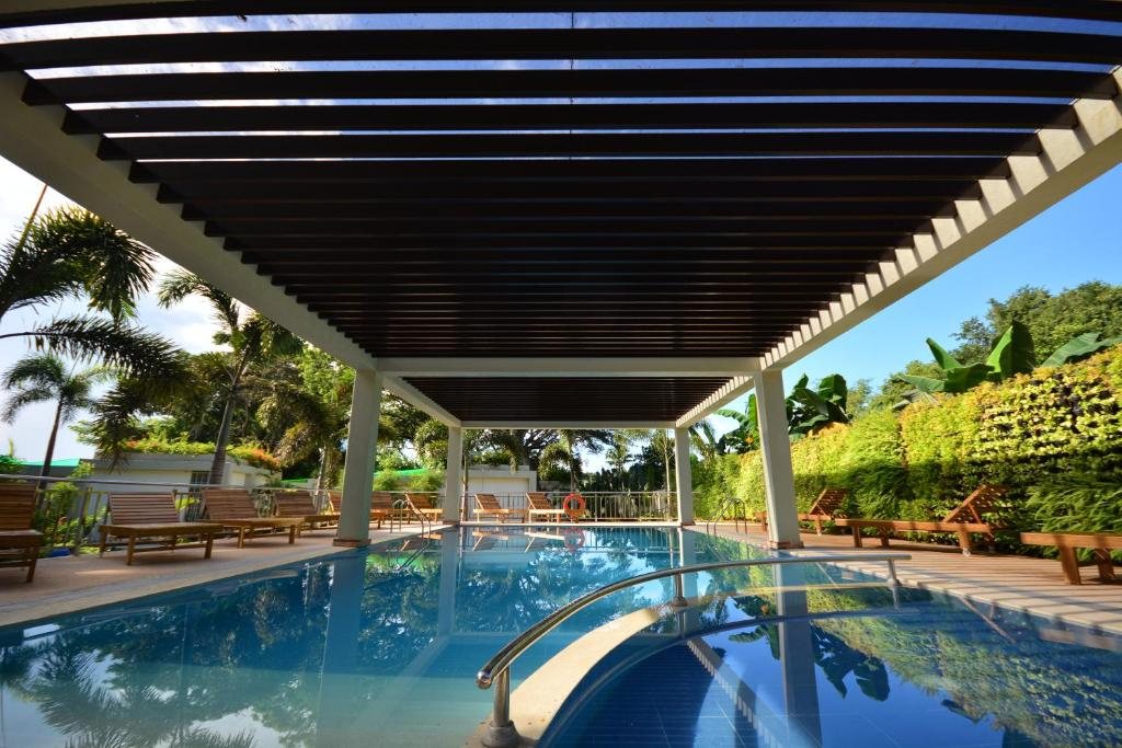 Outdoor swimming pool at Munting Paraiso under a wooden pergola with sun loungers and tropical garden