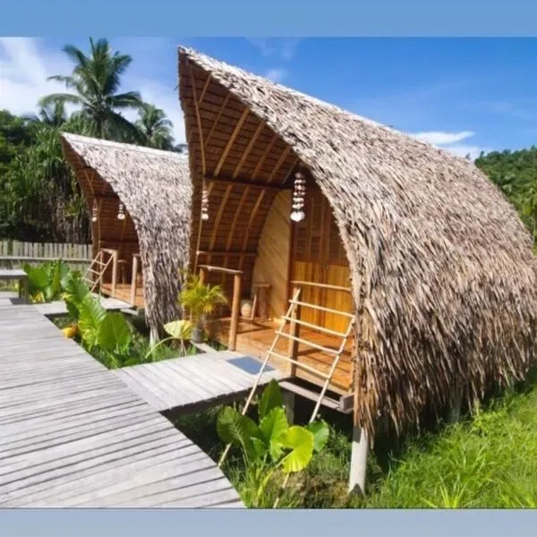 Row of curved cogon-thatch roof bungalows at The View - Jungle Lodges, Port Barton, connected by a raised wooden boardwalk through tropical garden planting
