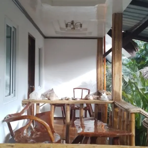 Covered porch at The View - Jungle Lodges, Port Barton, with a wooden table and chairs and decorative seashells, opening onto tropical garden