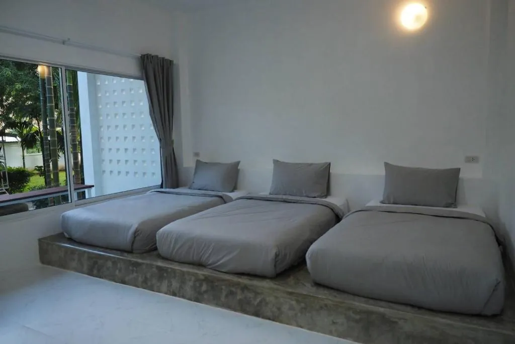 Triple room at Canary Guesthouse with three single mattresses side by side on a long concrete platform under a large window