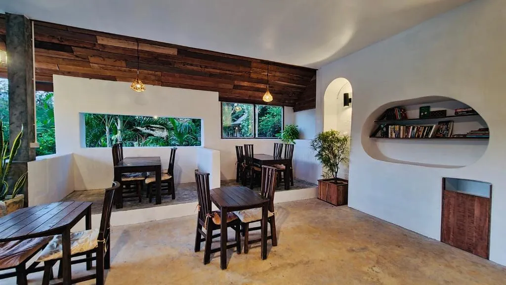 Indoor dining area at Canary Guesthouse with dark wooden tables, an arched bookshelf niche and windows onto the garden