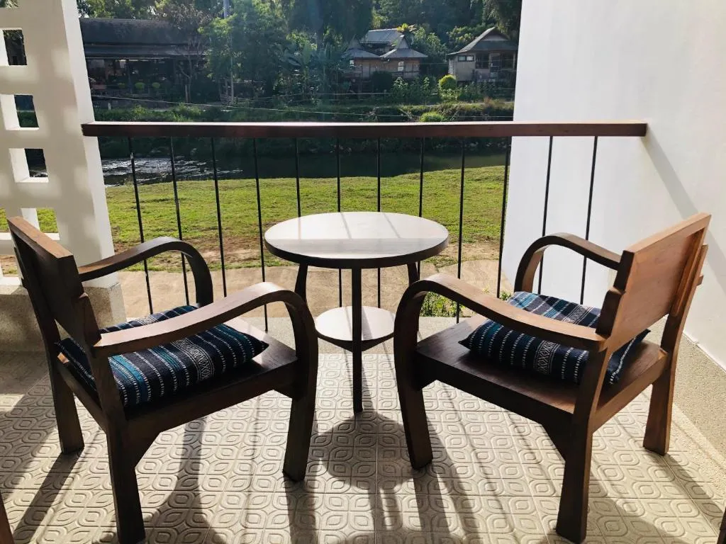 Private balcony at Canary Guesthouse with two wooden armchairs, striped cushions and a round table overlooking the garden