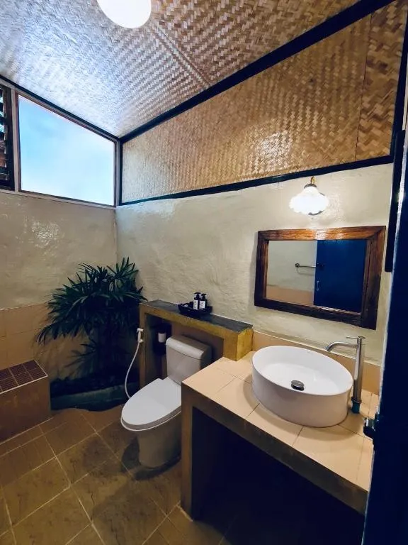 Bathroom at Canary Guesthouse with a vessel sink on a wooden vanity, woven bamboo ceiling panel and potted plant