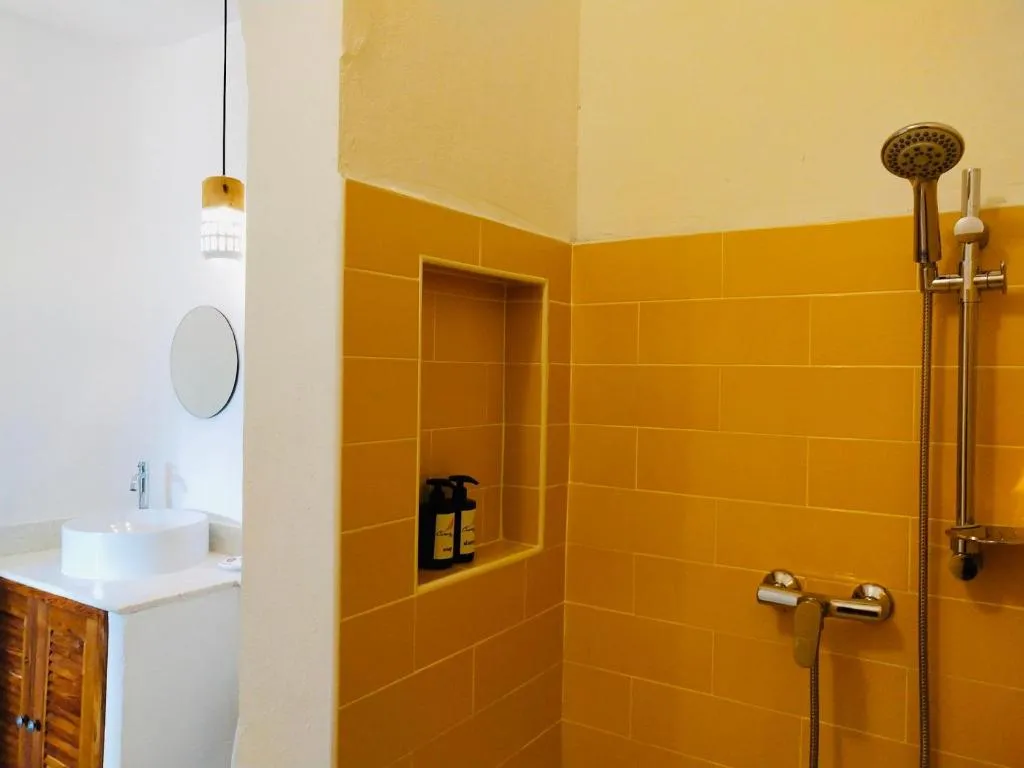 Walk-in shower at Canary Guesthouse with mustard-yellow tiles, rain shower head and a built-in niche with toiletries