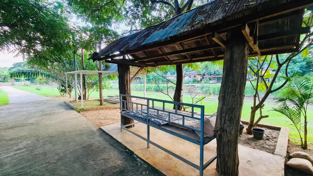 Thatched riverside shelter with a blue bench along a garden walkway at Canary Guesthouse