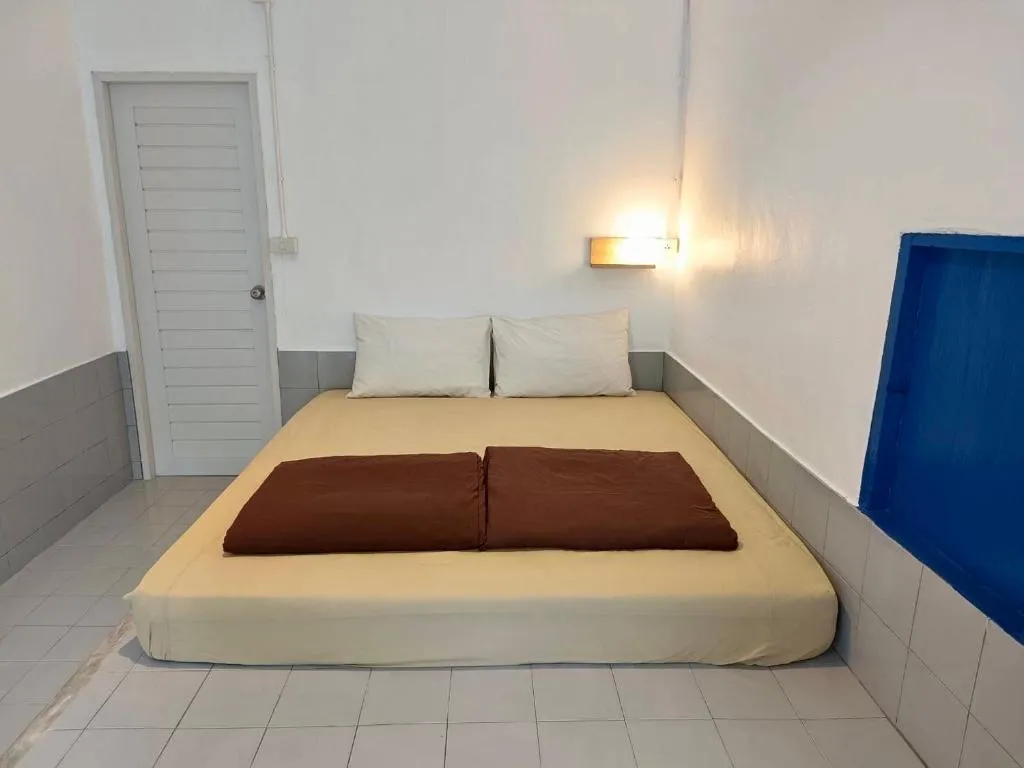 Simple room at Canary Guesthouse with a low double mattress, brown throw, wall lamp and blue window frame