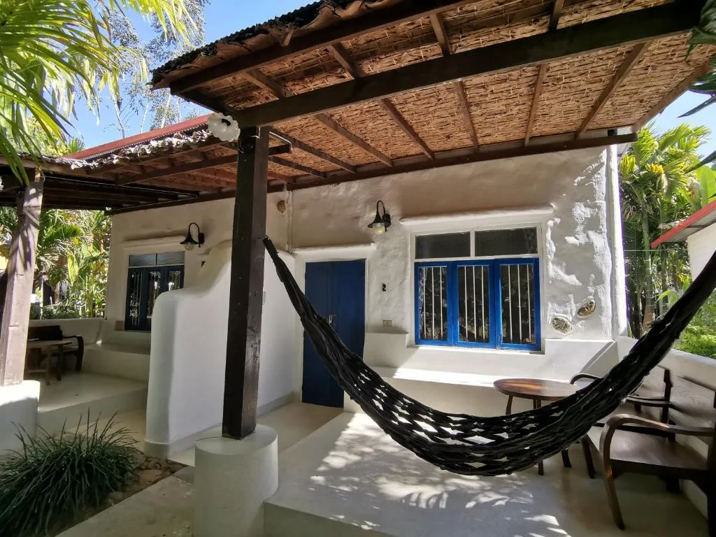 White garden bungalow at Canary Guesthouse with a thatched veranda, hammock, blue shutters and wooden armchair