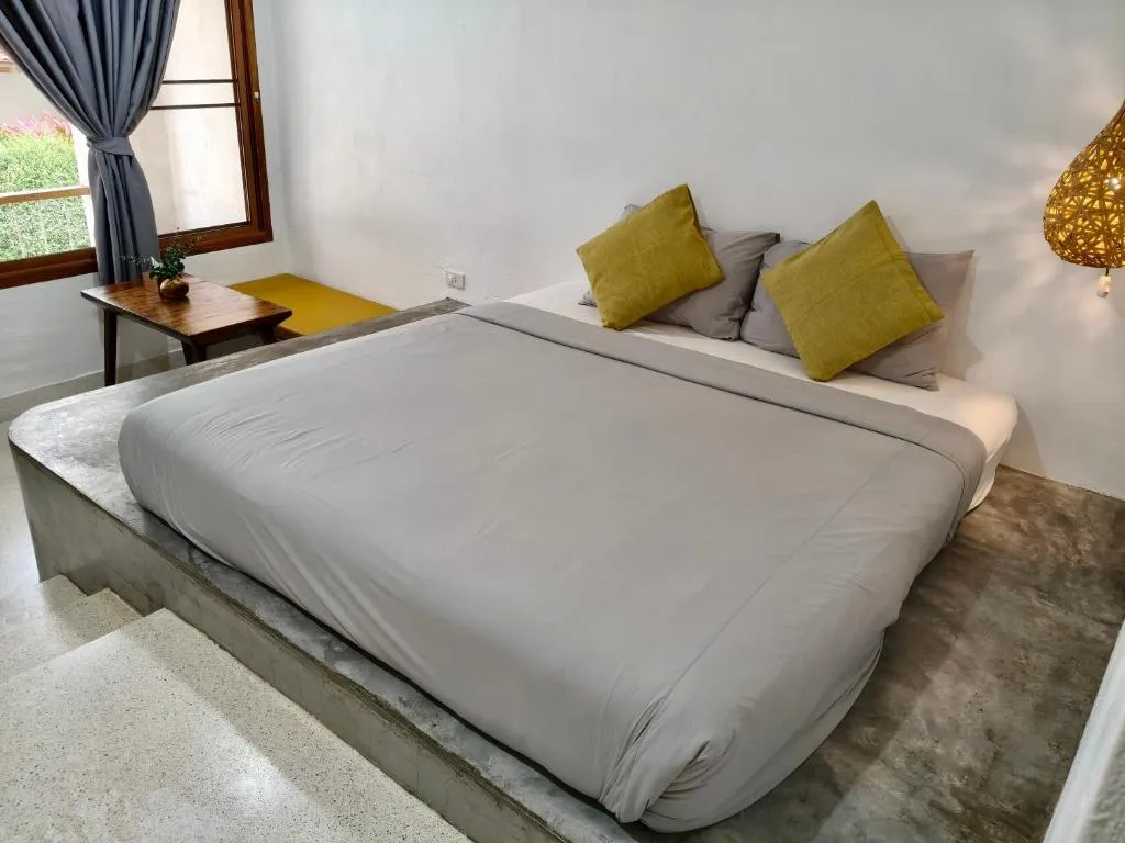 Bright room at Canary Guesthouse with a large bed on a polished concrete platform, mustard cushions and wooden window