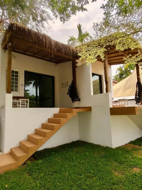 Stilted white room at Canary Guesthouse with wooden stairs, a thatched patio roof and lawn in front