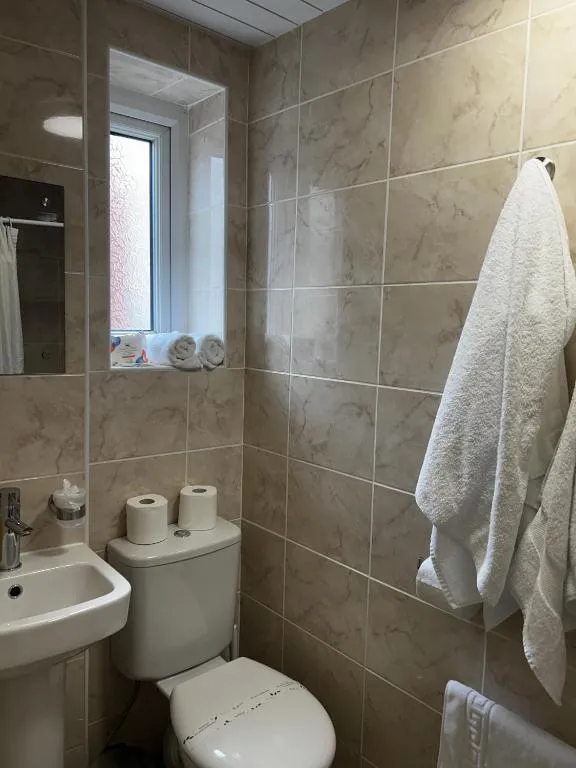 Tiled en suite at The Inglewood Hotel with a pedestal basin, toilet, heated rail and a white bathrobe hanging by the shower