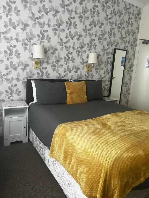 Double bed with mustard cushions and throw against silver leaf-pattern wallpaper with wall lights at The Inglewood Hotel
