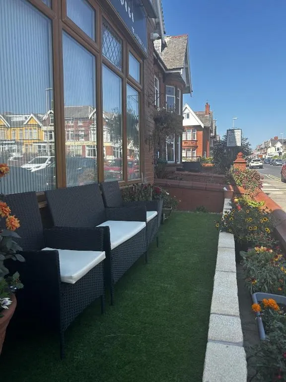 Artificial-grass front terrace of The Inglewood Hotel with black rattan seating and planters, looking along the terraced houses of Holmfield Road