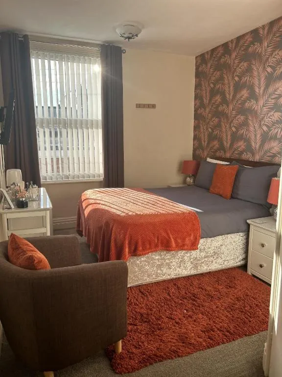 Room at The Inglewood Hotel with a burnt-orange throw and cushions, tropical-leaf feature wall and a brown armchair