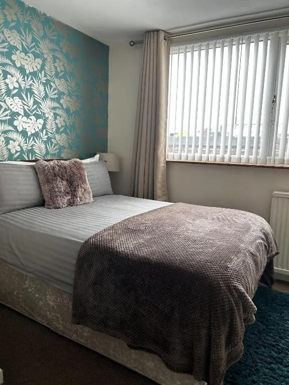 Double room at The Inglewood Hotel with a teal botanical feature wall, striped white bedding and a mink-coloured throw