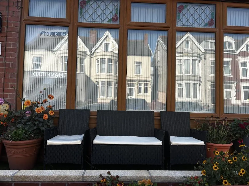 Black rattan sofa with white cushions under the leaded bay windows of The Inglewood Hotel, framed by orange and red flower pots