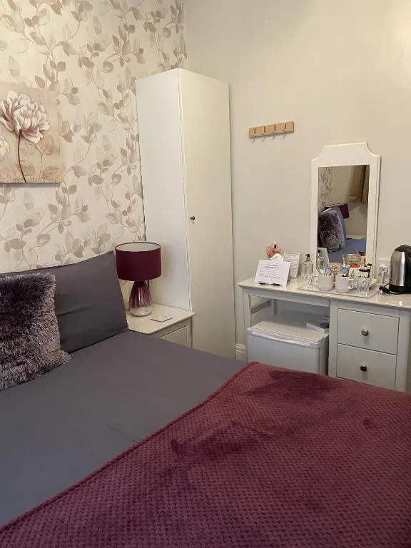 White dressing table with a mirror, kettle and hospitality tray beside a double bed with a plum throw at The Inglewood Hotel