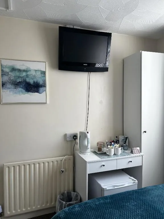 Desk with kettle, mugs and tea tray, a mini fridge underneath, a wall-mounted TV and white wardrobe in a room at The Inglewood Hotel