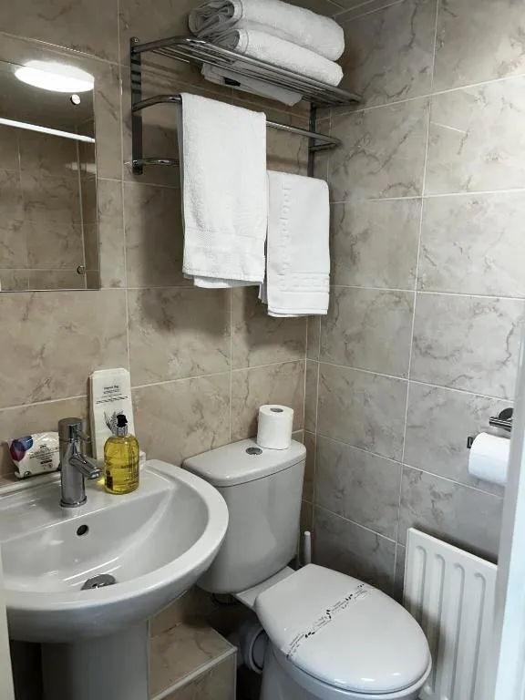 En suite at The Inglewood Hotel with a pedestal basin, hand wash, toilet and a chrome shelf of fresh white towels