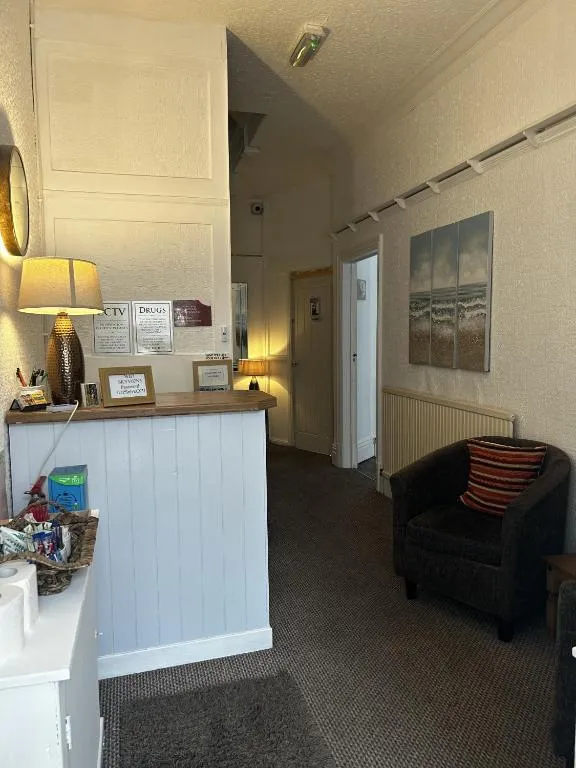Small white reception desk with a table lamp and an armchair in the carpeted entrance hall of The Inglewood Hotel