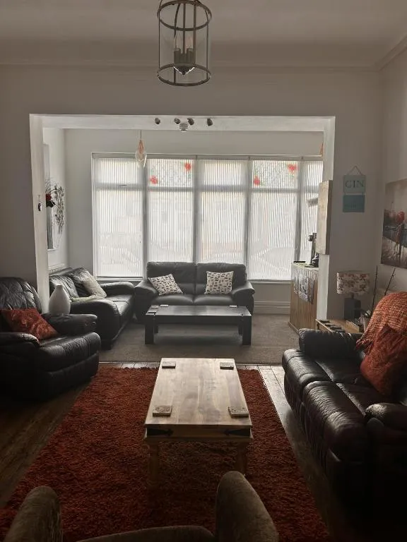Shared guest lounge at The Inglewood Hotel with dark leather sofas, a red rug, a wooden coffee table and a wide bay window