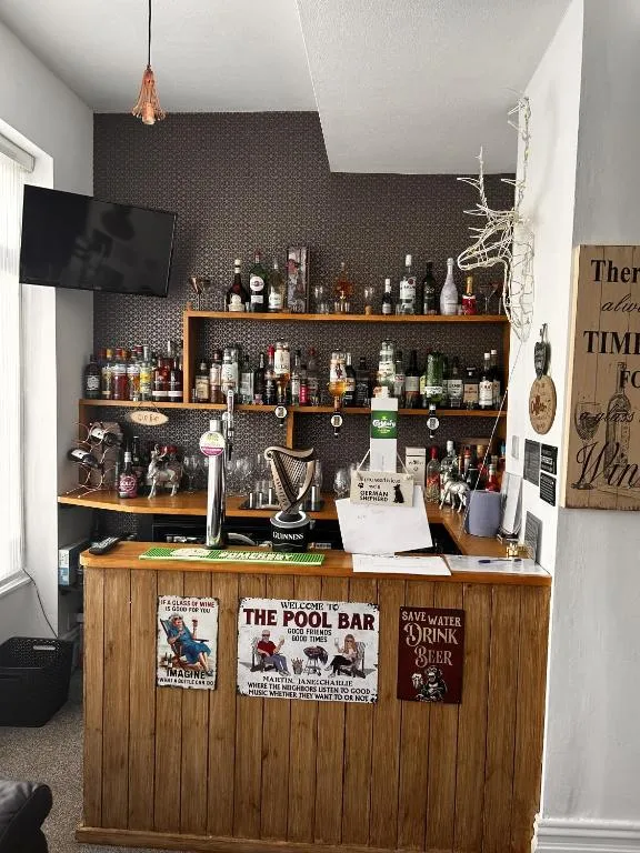 Wooden honesty bar counter at The Inglewood Hotel with draught taps, shelves of spirits and a wall-mounted TV in the guest lounge