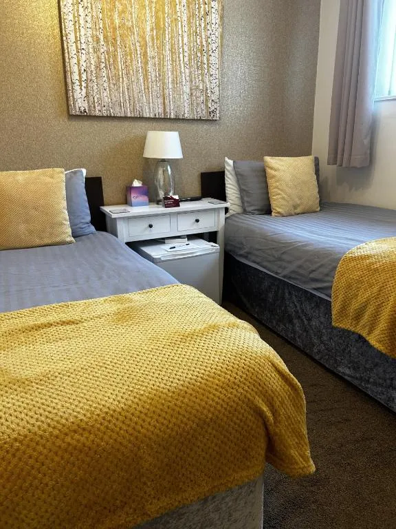 Twin room at The Inglewood Hotel with two single beds in grey linen and mustard throws, a white bedside table and birch-tree wall art